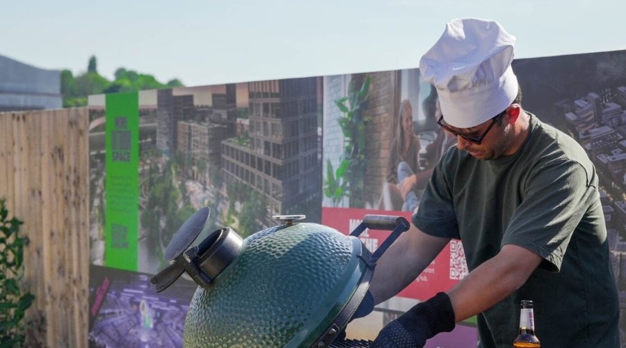 Man wearing chefs hat grills sausages on a sunny afternoon on The Green at Brabazon, Bristol.