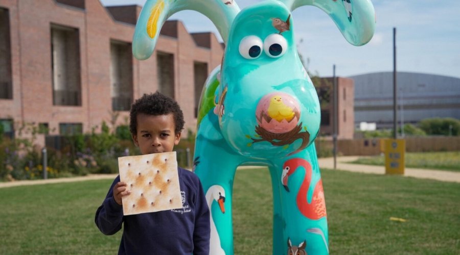 Young boy holding cardboard cut-out of a cracker next to 'The Birds' Gromit on The Green at Brabazon.