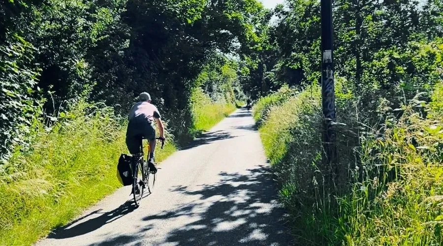 Male cyclist with pannier cycling along the green Bristol to Bath cycle path on a sunny day.
