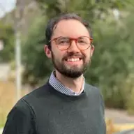 Jonny Verrell Close up photograph of a smiling young man with brunette hair and glasses