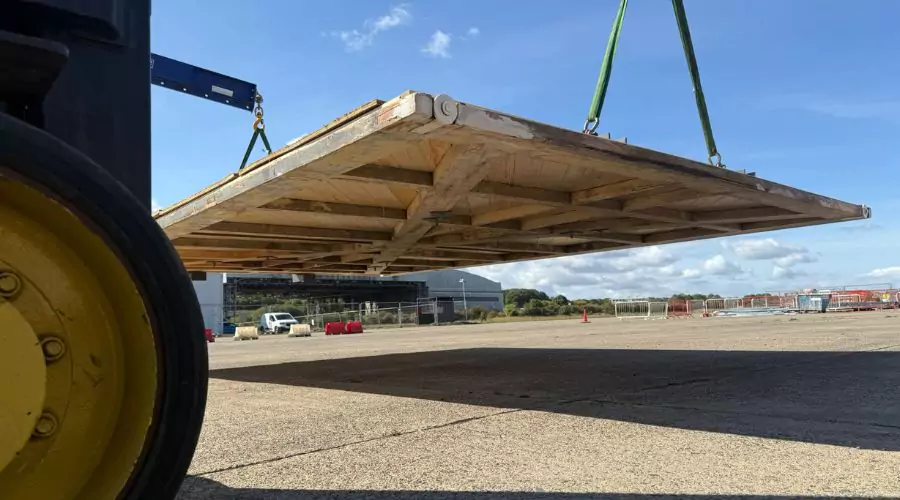 large wooder fully restored doors from former Hangar 16U is suspended from a forklift on the former Filton Airfield area, with historic hangar in the background.