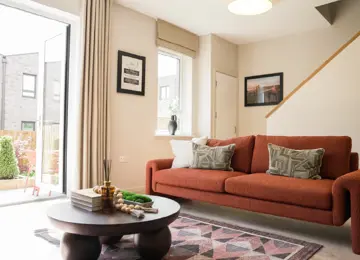Modern living room featuring a rust-coloured sofa with patterned pillows, a round coffee table, and large windows opening to a garden.