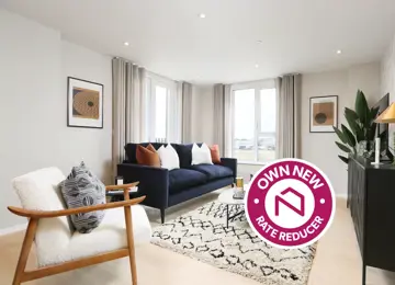 Own New Rate Reducer sticker overlaying wide angle view of apartment living room at The Dials, featuring a navy sofa a white arm chair and black and white rug covering wooden flooring. 