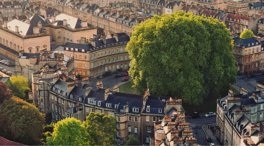 Aerial view of historic Georgian townhouses in Bath, built around a roundabout with a large, lush green tree.