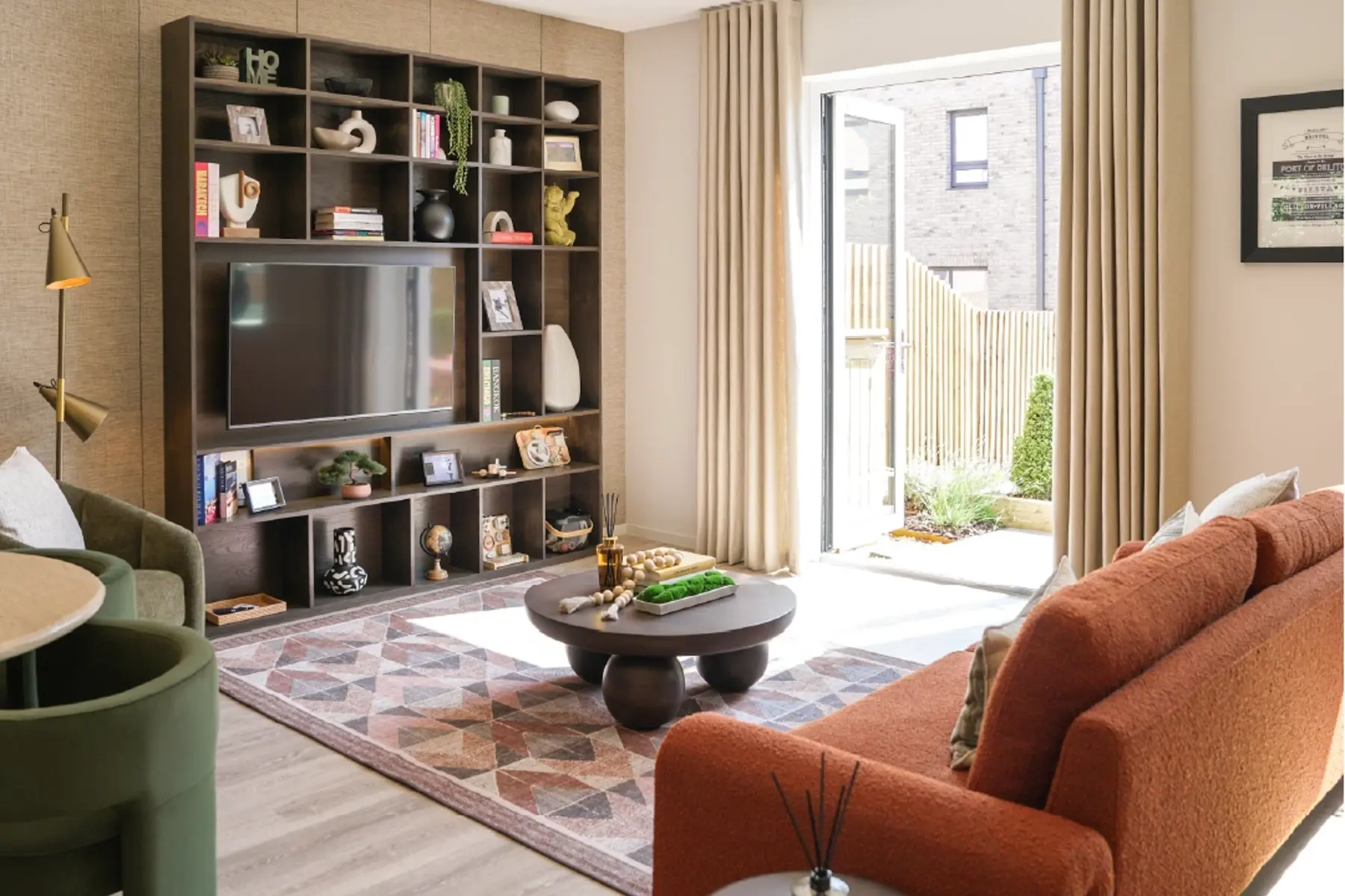 Modern living room featuring a custom TV shelp, orange sofa, patterned rug, and natural light streaming in through open doors.