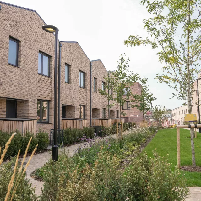 A row of modern, new, terraced brick houses fronting onto a landscaped green living street at Brabazon in Bristol.