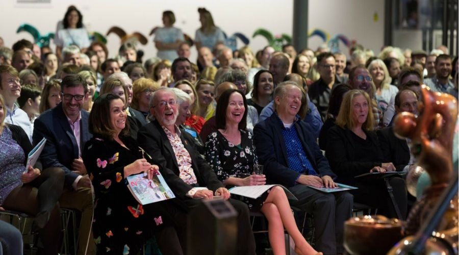 Crowd of people seated in function room, smiling.