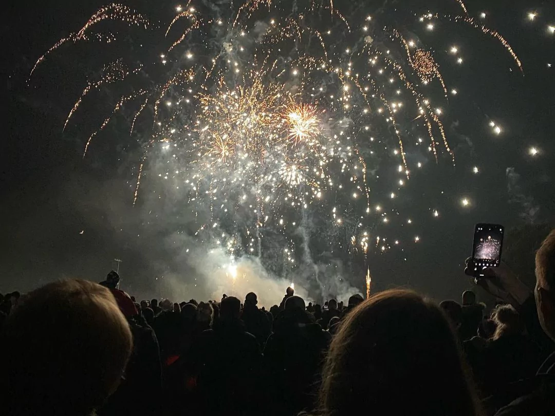 White and yellow fireworks exploding over the heads of a busy crowd