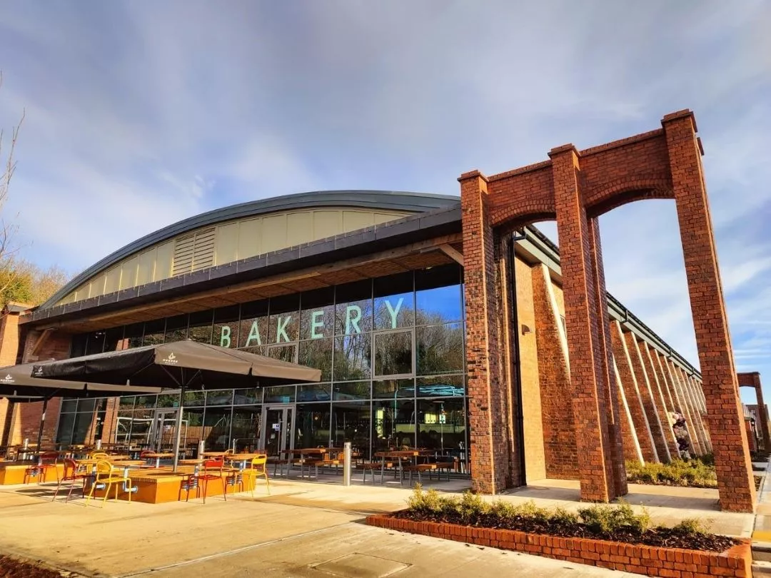 Exterior of Spitfire Hangar featuring 'Bakery' sign with large glass windows, with outdoor seating with umbrellas. 