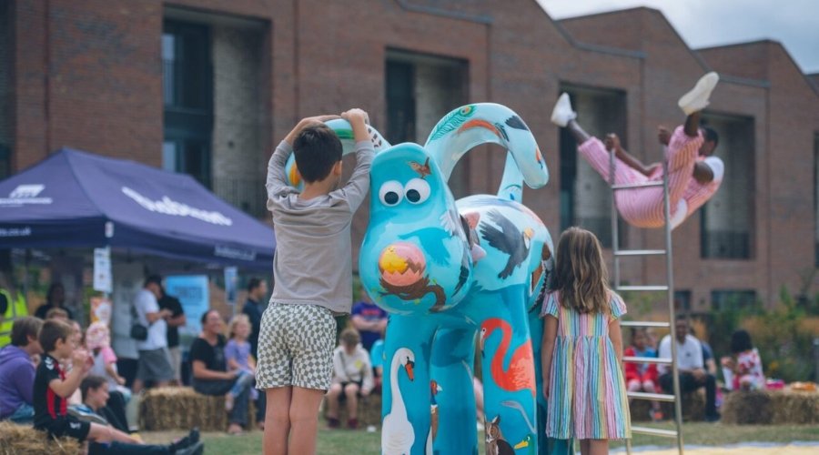 Children stand next to Gromit 'The Birds' sculpture while watching Circus Performers on The Green at Brabazon.