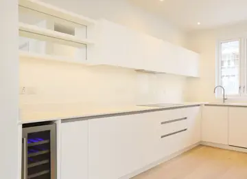 A sleek white kitchen with integrated hob and wine fridge and wood flooring.