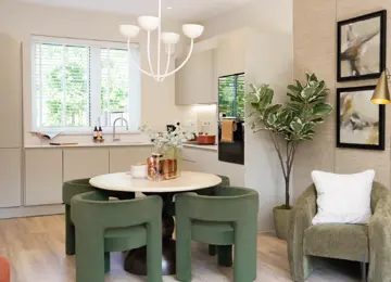 A modern, bright kitchen-dining area at The Coanda Show Home, featuring a round table with green chairs, modern appliances, and large windows with greenery visible outside.