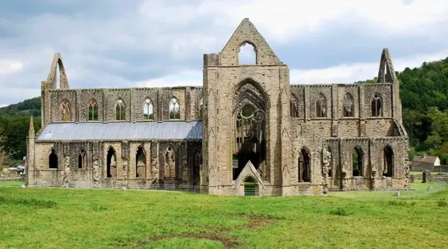 The ruins of Tintern Abbey surrounded by green grass on a bright and dry but cloudy day.