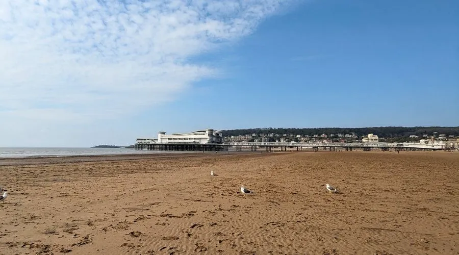 A sunny day at Weston-super-Mare beach, showing a long stretch of golden sand leading to the historic pier.