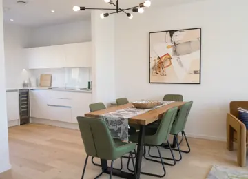 Modern and light dining and kitchen area, with light wooden flooring, modern dining table with green chairs. 