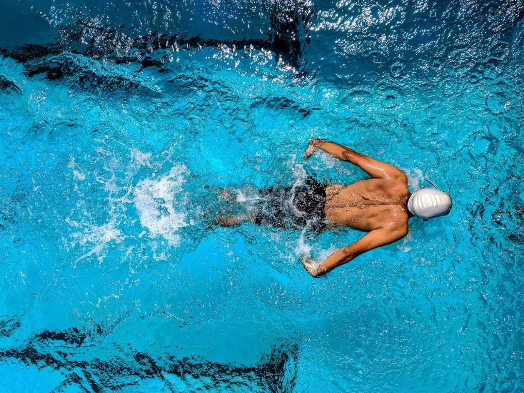 Muscular male swimmer in swimming hat doing butterfly stroke in a swimming pool