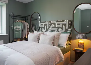 Cozy and modern secondary bedroom at Brabazon, with white bedding and a cool teal wallpaper. 
