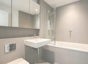 A family bathroom with mirrored bathroom cabinets and bath tub.