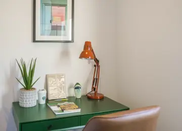 Green desk with potted plant, orange lamp and leather chair in secluded study in The Burney at Brabazon. 