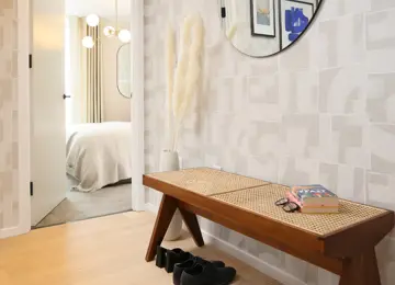 A lovely shot of the apartment hallway featuring a stylish rattan bench and a vase including cream pampas grass whilst sneaking a glimpse into the primary bedroom.