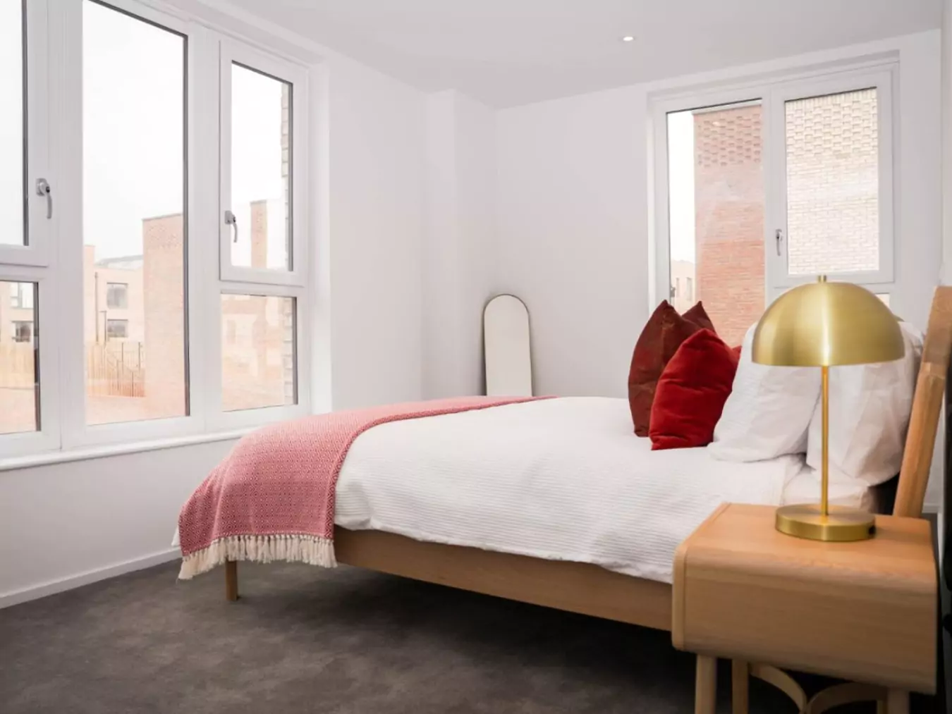 Bright, modern bedroom in apartment at Brabazon with a large bed, decorative pillows, a red throw, and a stylish gold lamp.