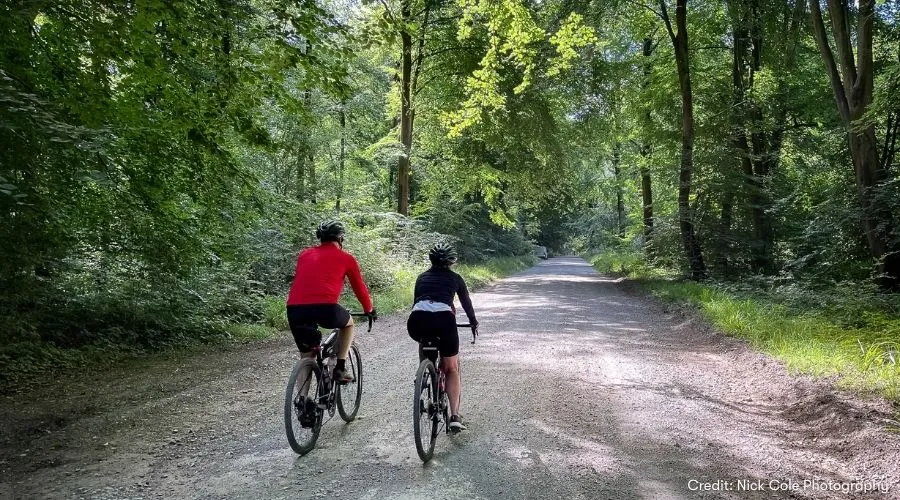 Two cyclists cycling along the Bristol to Bradford on Avon bike path under the shade of the trees.