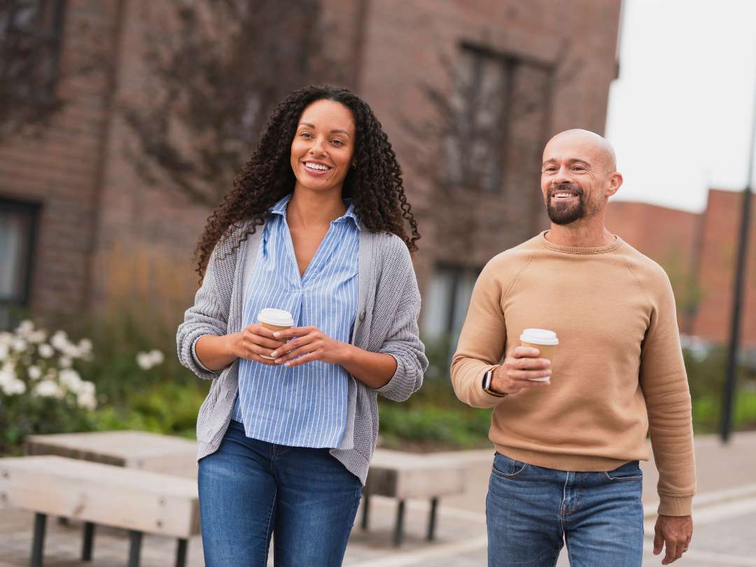 Young couple smiling and walking with takeaway coffee cups