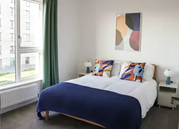 A bright guest bedroom with a generous window and furnished with a double bed with bedside tables.