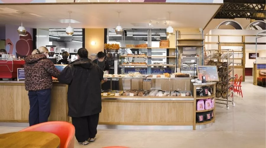 Inside Mokoko Bakery at Spitfire Hangar, North Bristol, featuring two customers at the counter, displaying pastries and bread. 
