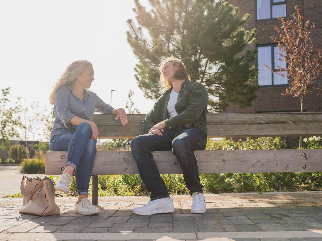 Older female and young male laughing and smiling on a wooden bench in the sun